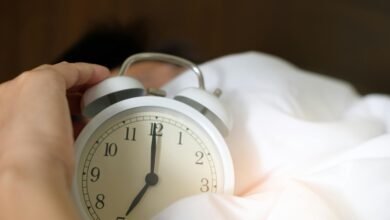 A close-up of a hand reaching for a ringing alarm clock, symbolizing waking up in the morning.