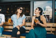 Two women laughing and enjoying drinks outdoors at a trendy bar, creating a vibrant and social atmosphere.