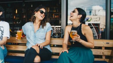 Two women laughing and enjoying drinks outdoors at a trendy bar, creating a vibrant and social atmosphere.