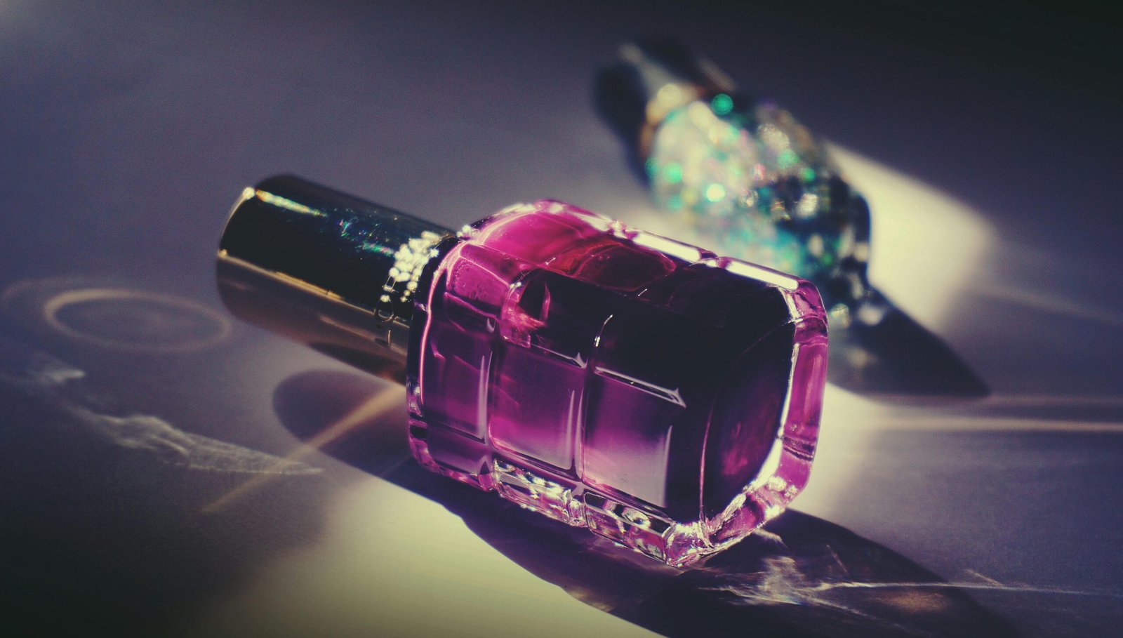 Artistic close-up of a pink nail polish bottle with reflective light and vivid colors.