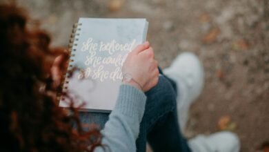 A woman holds a notebook with an inspirational quote, sitting outdoors.