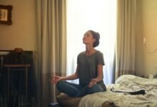 Adult woman practicing meditation on her bed surrounded by a calm bedroom atmosphere.