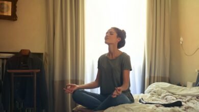 Adult woman practicing meditation on her bed surrounded by a calm bedroom atmosphere.