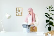 A woman wearing a hijab stands at a desk, organizing documents in a modern, minimalist office setting.