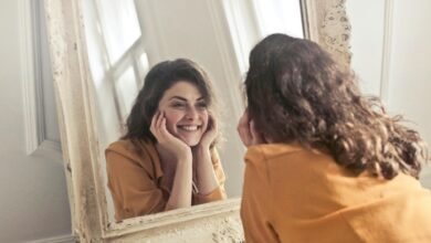 A cheerful woman smiles at her reflection in a vintage-style mirror, exuding positivity and warmth.