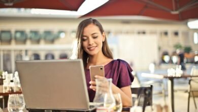 Woman enjoying remote work at a café, using a laptop and smartphone.